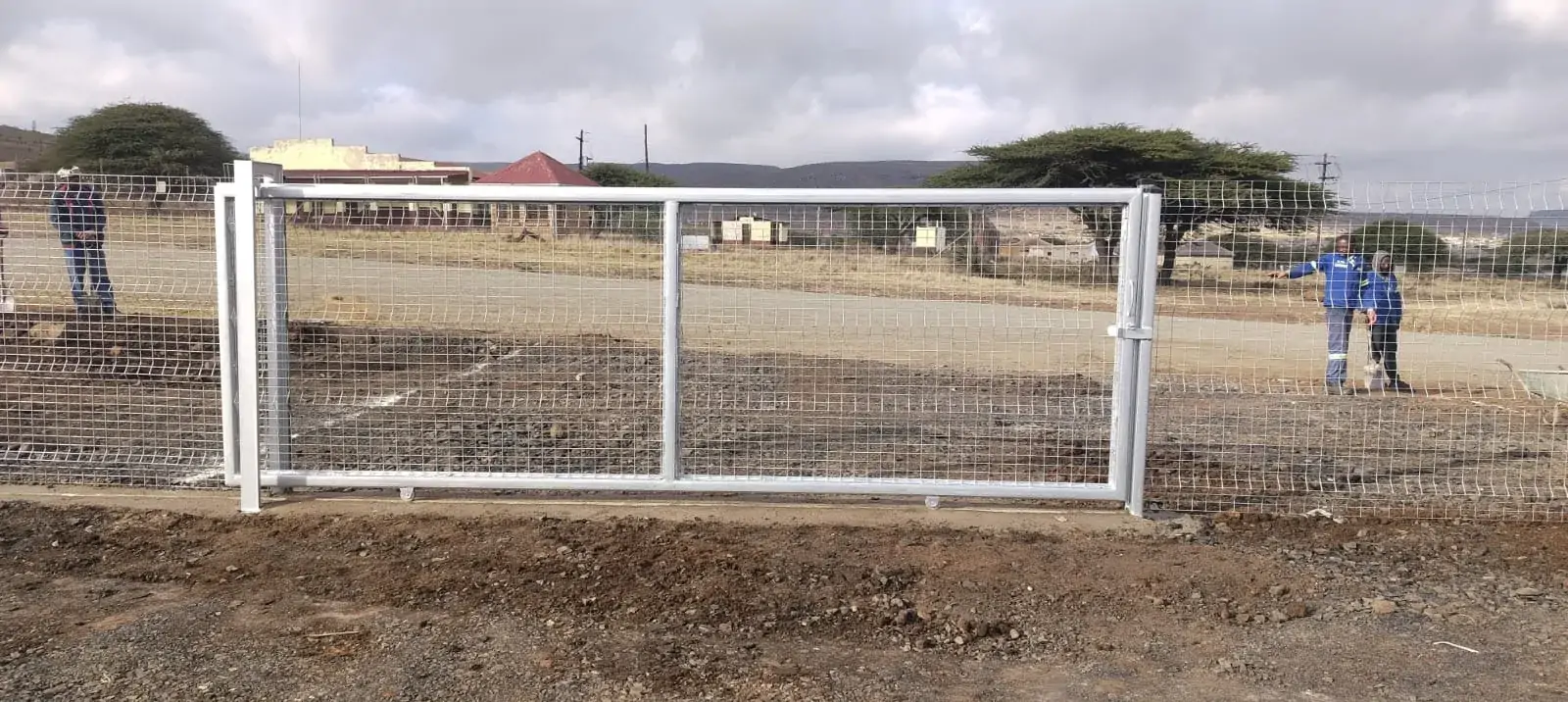Wide vehicle gate with installers beside the adjoining mesh fence