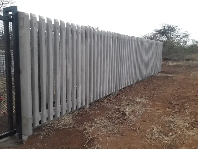 Completed concrete palisade boundary beside a cleared strip of ground